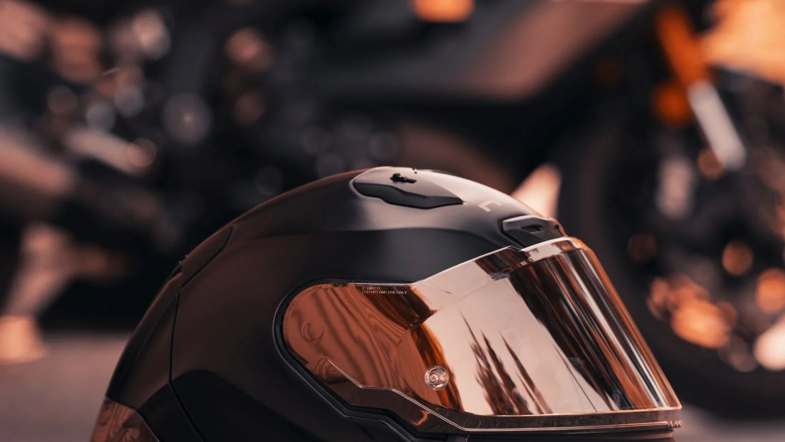 Capacete de motociclista sobre o asfalto com uma moto ao fundo
