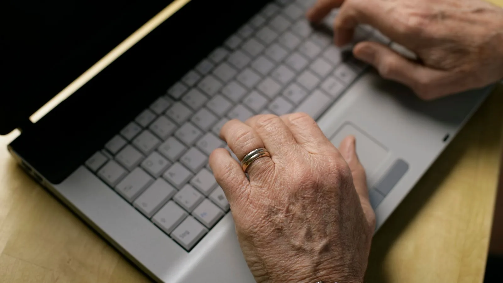 Mãos de uma pessoa idosa digitando em um notebook